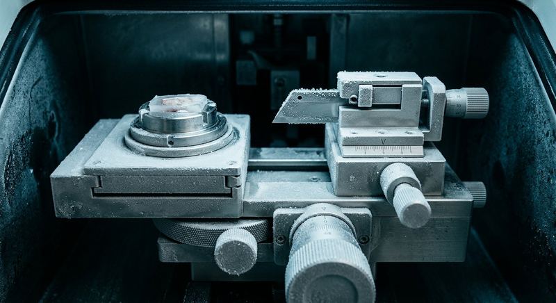 The frost-covered interior of a cryostat microtome showing the blade holder and specimen stage
